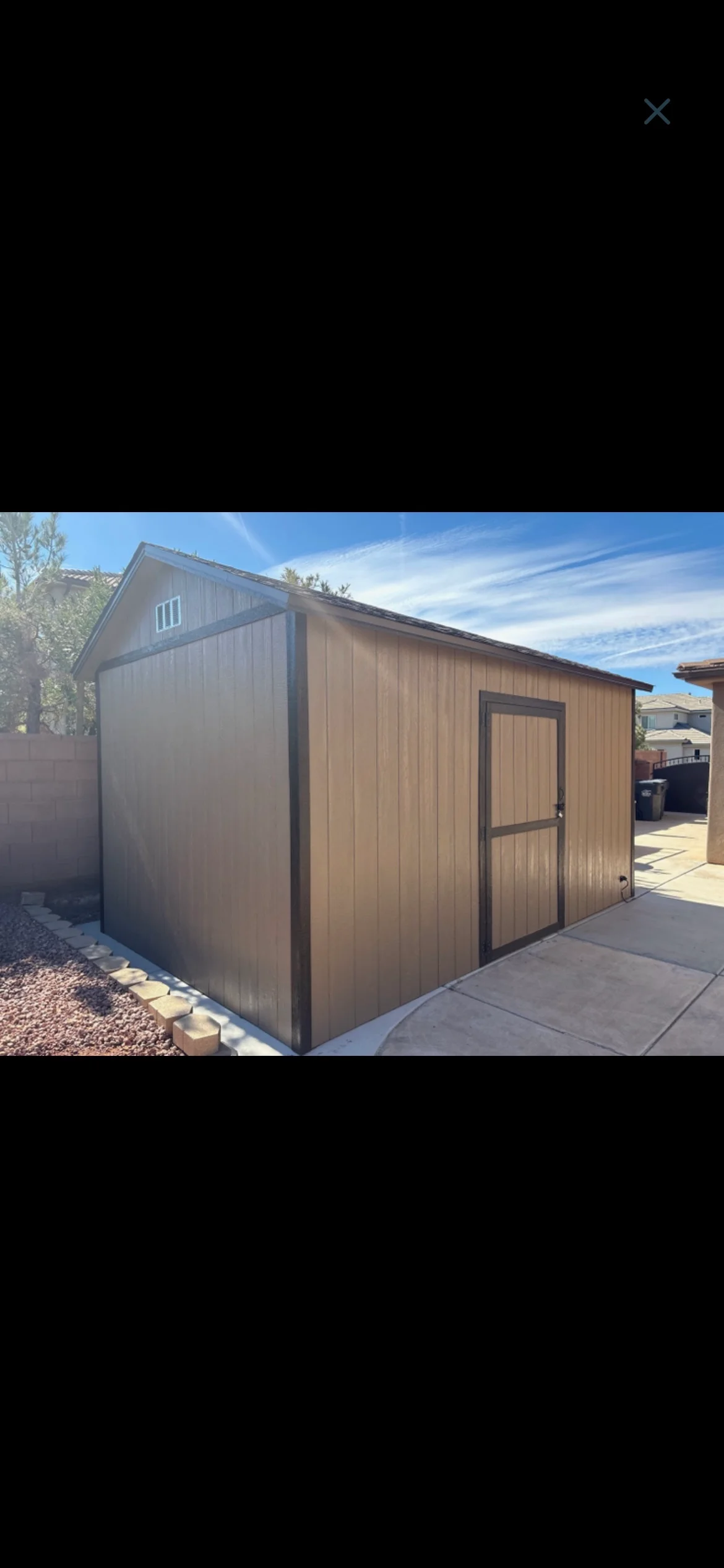 Tan and brown gable shed with single door and dark trim installed in a residential backyard by Quality Creations