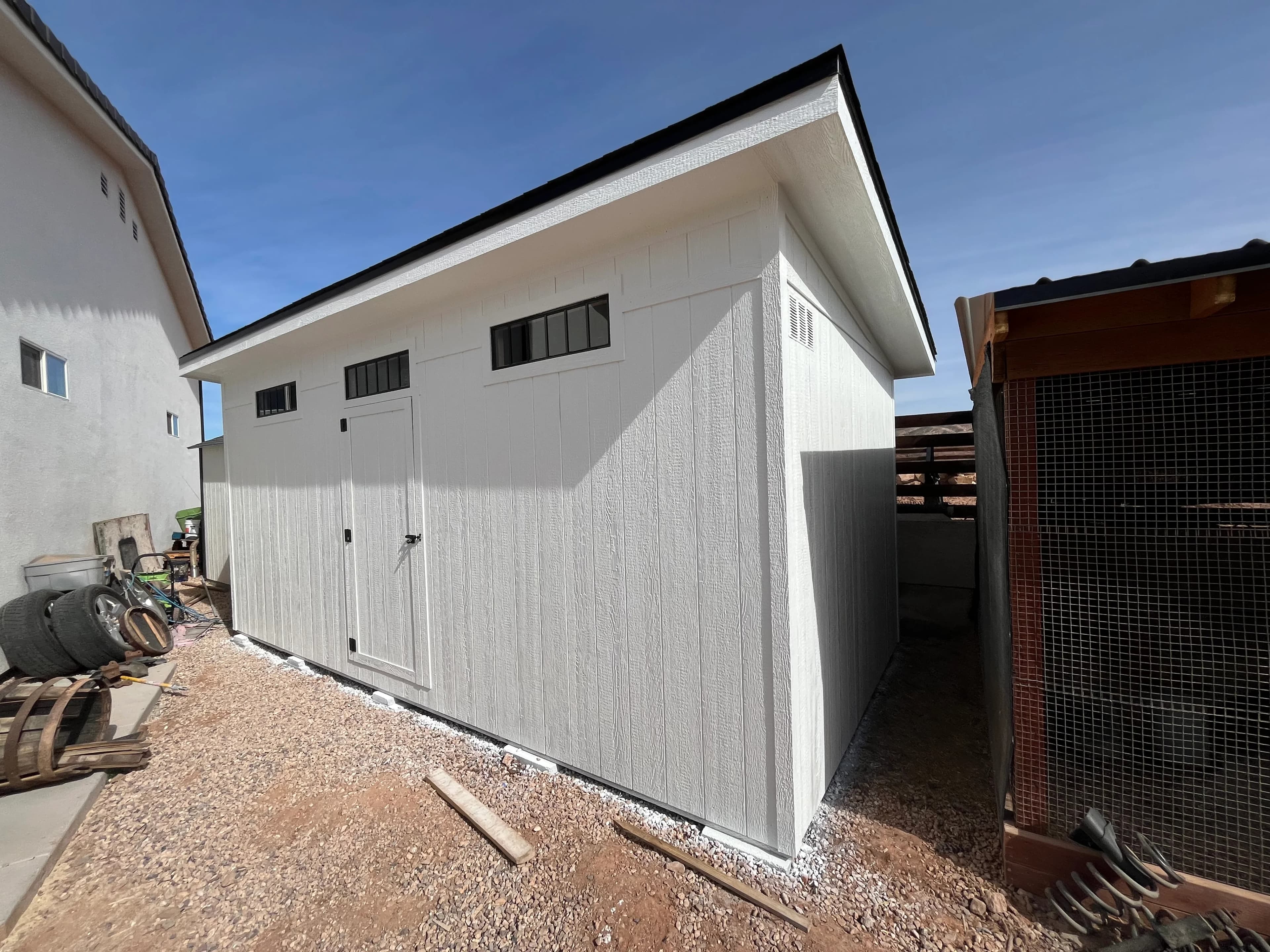 Corner view of white modern shed with black roof edge and horizontal transom windows on a residential property