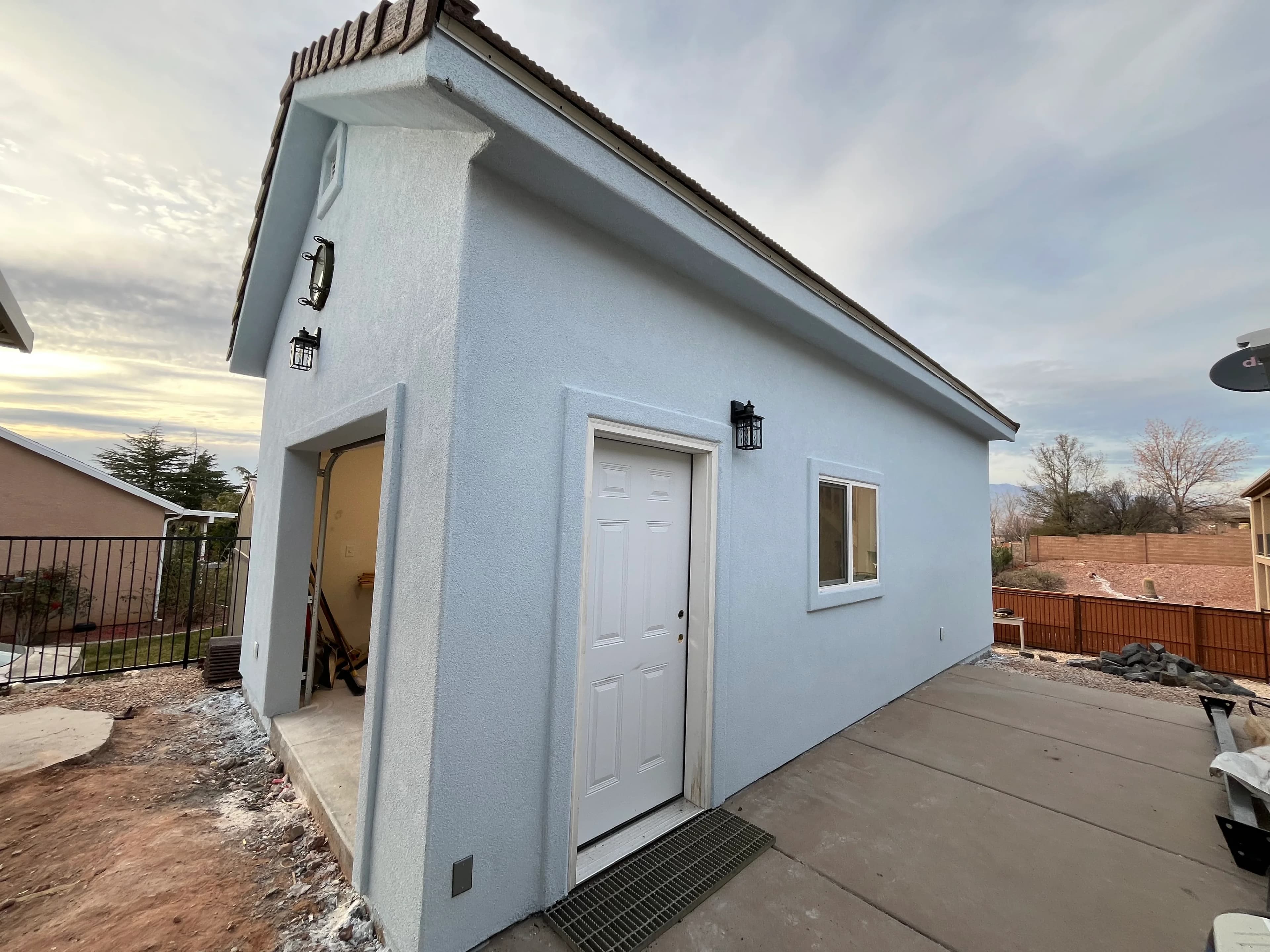 Quality Creations white stucco garage with entry door, window, and decorative lanterns at dusk