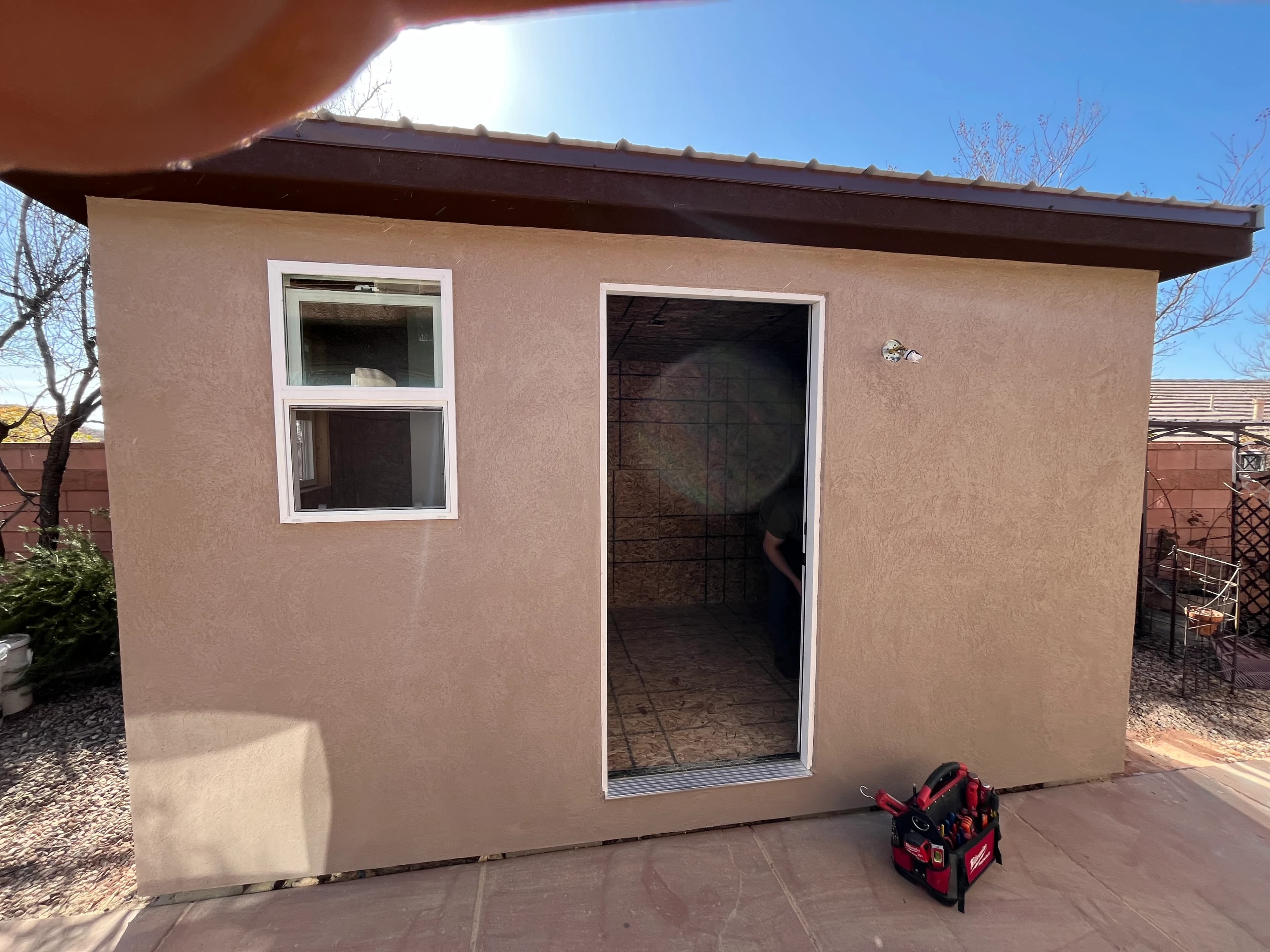 Quality Creations stucco shed with flat roof, white entry door, and window on a desert backyard lot