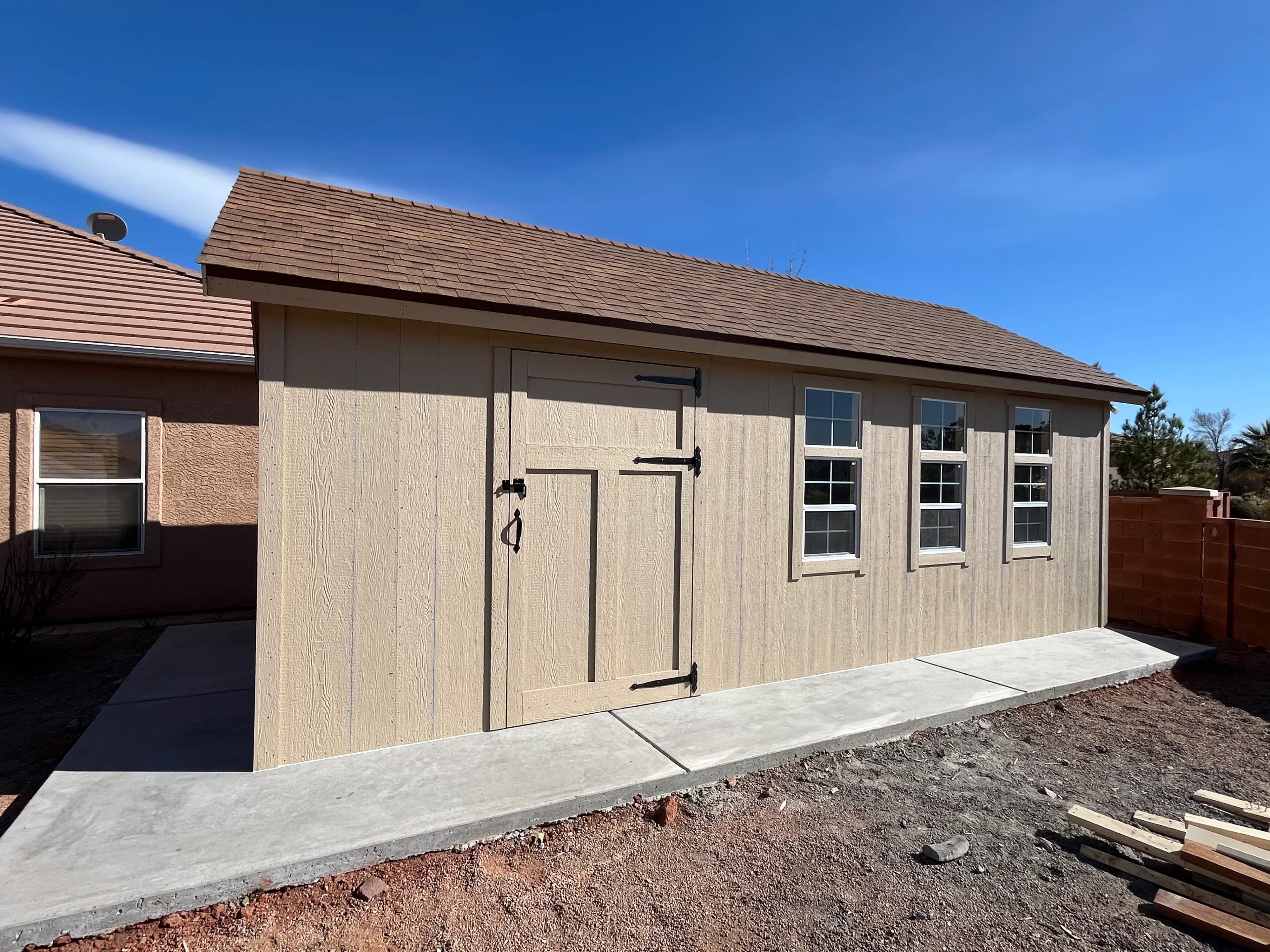 Long tan shed with single entry door and three windows on a concrete pad in Southern Utah backyard