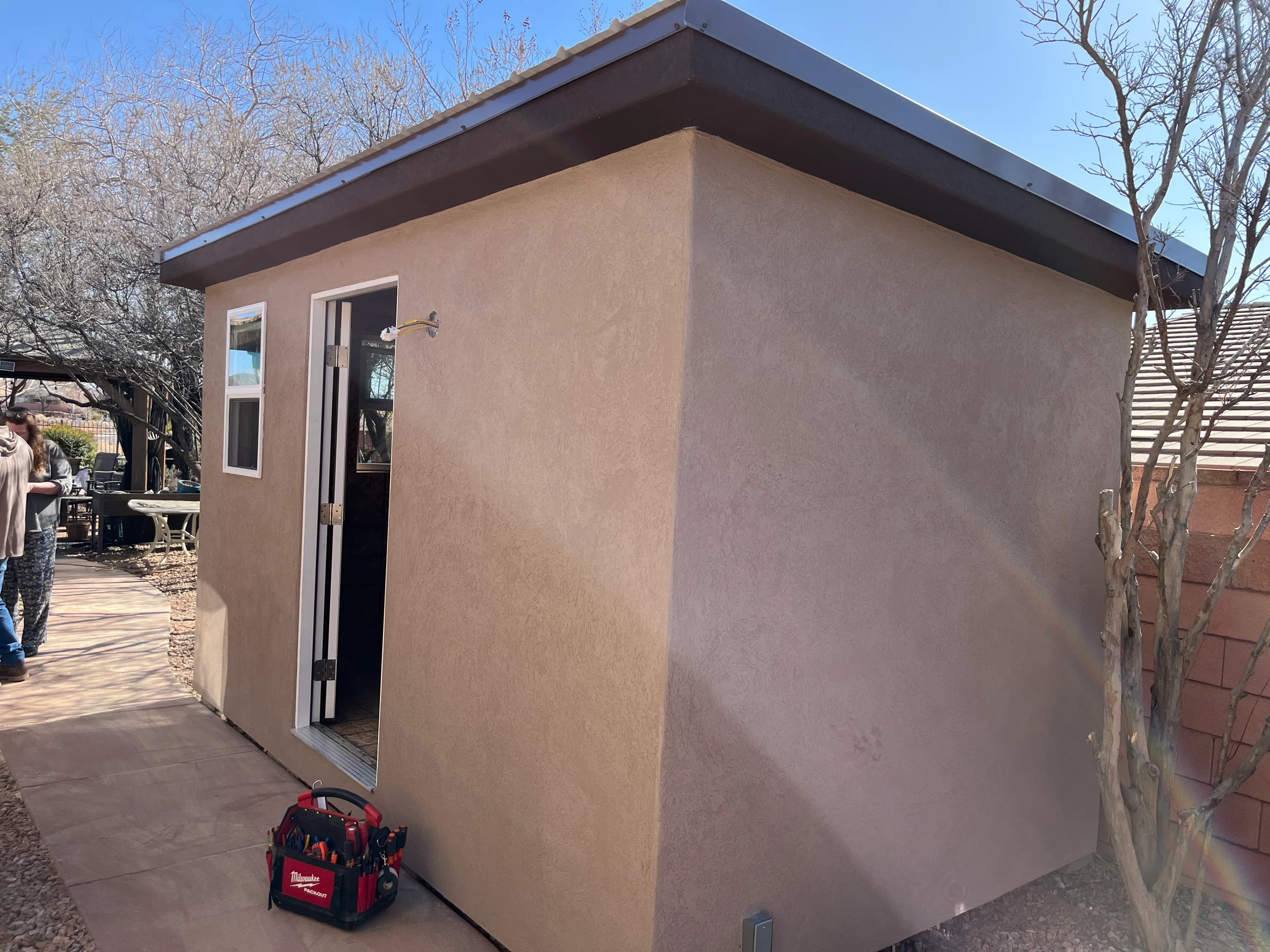 Compact stucco shed with flat roof and entry door under construction in a residential backyard