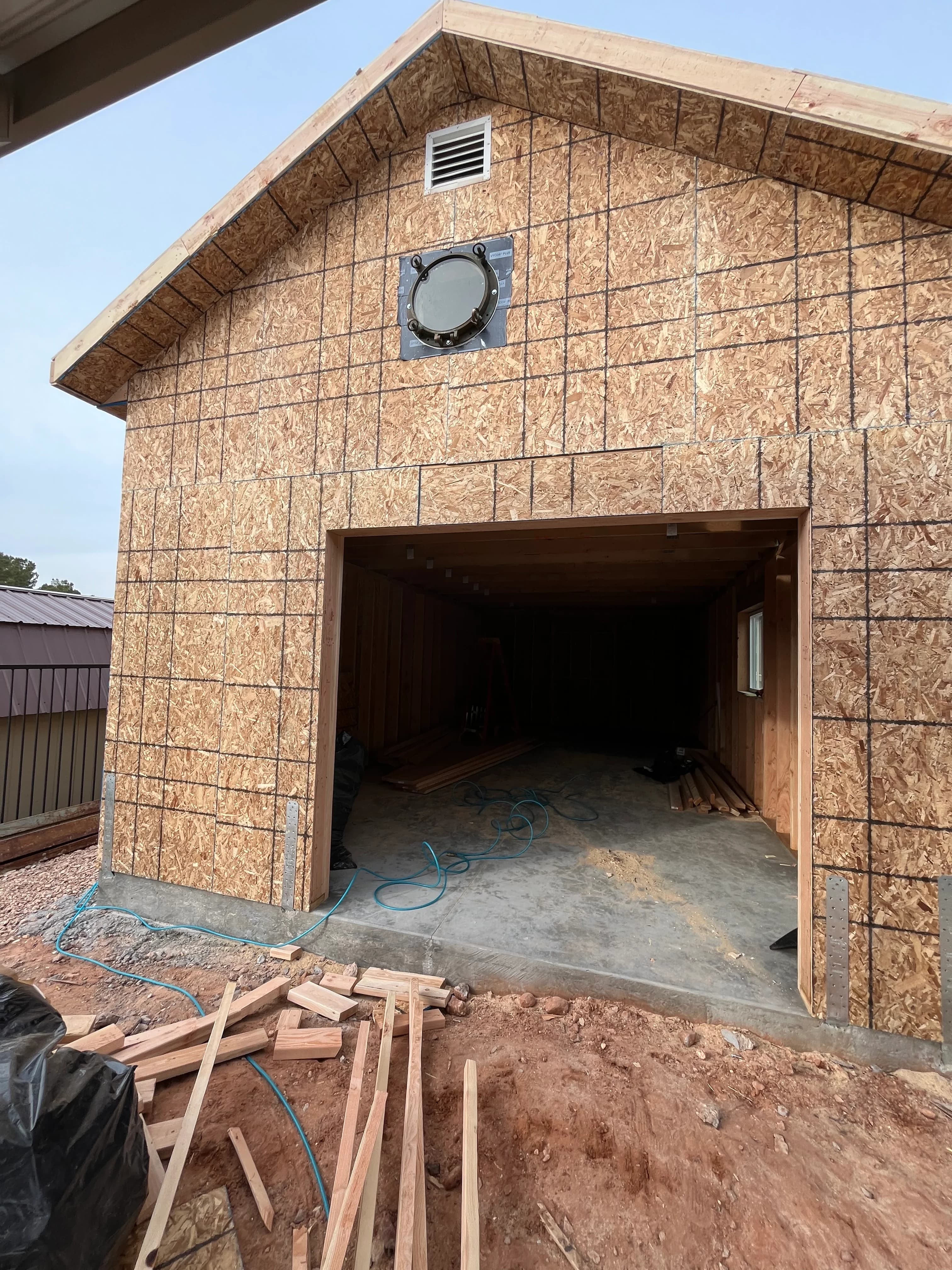 Front view of a detached garage framed with OSB sheathing, porthole window, and wide vehicle bay opening