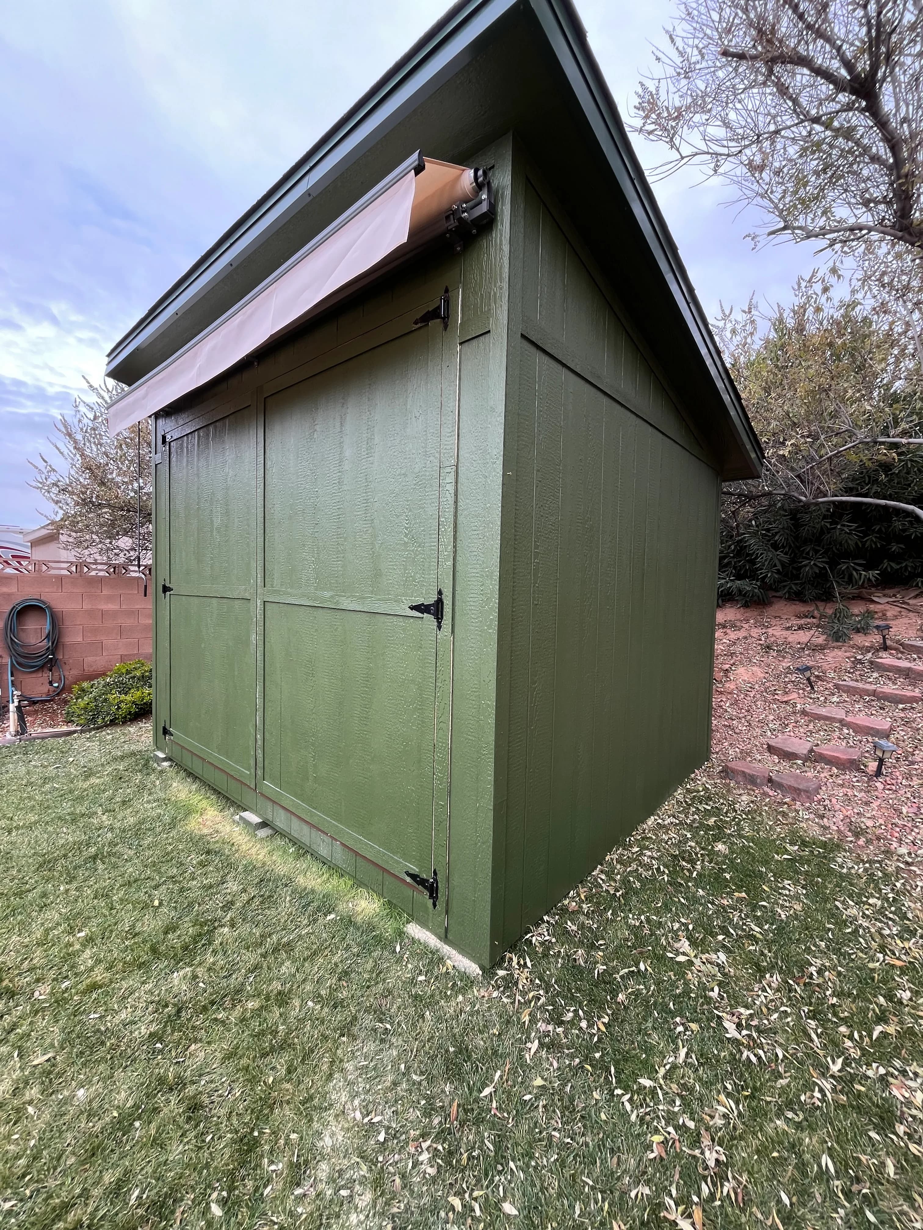 Side angle of a green lean-to style shed showing the steep single-slope roofline and board-and-batten siding
