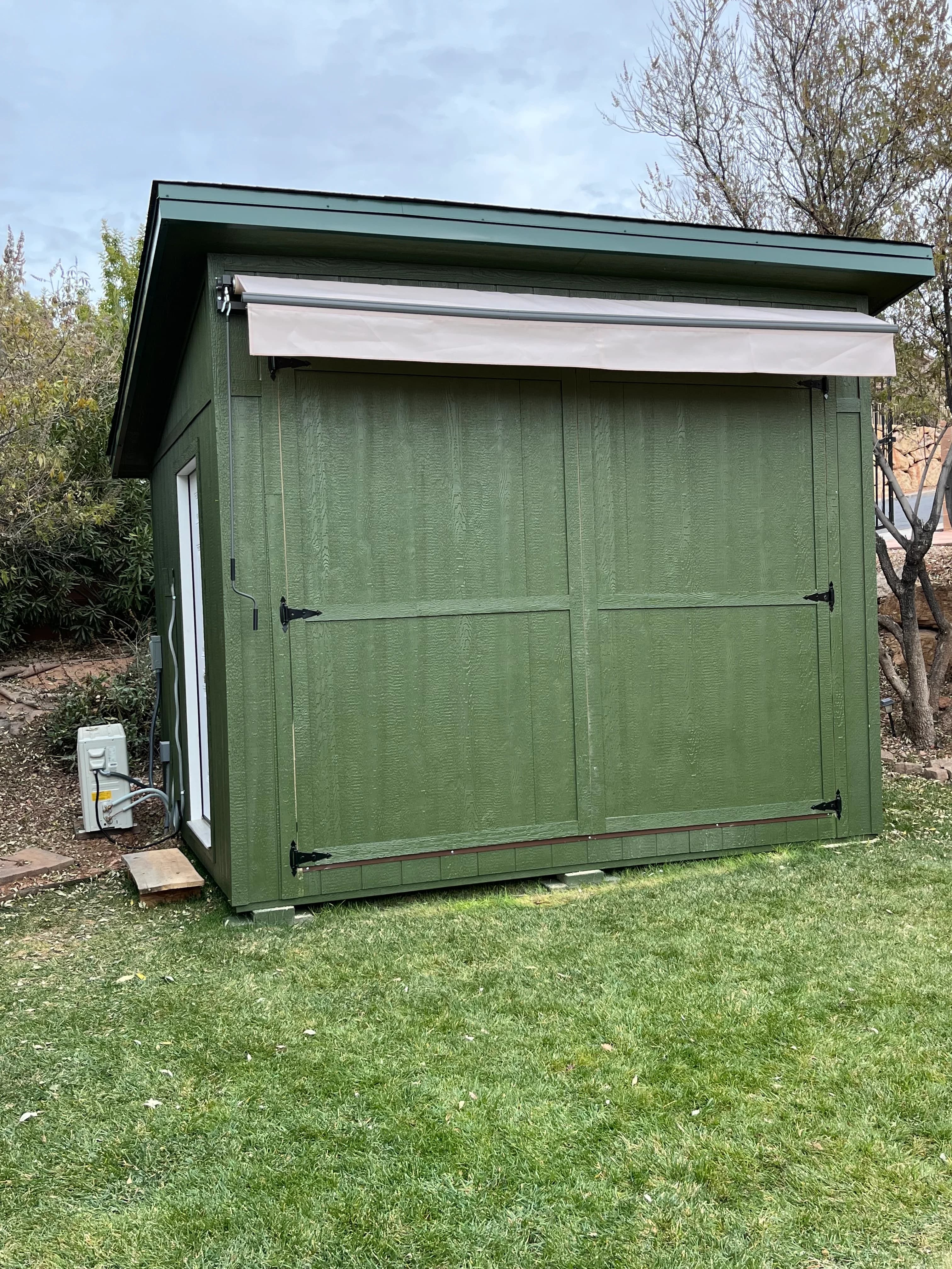 Green lean-to shed with double barn doors and metal roof built by Quality Creations in a Southern Utah backyard