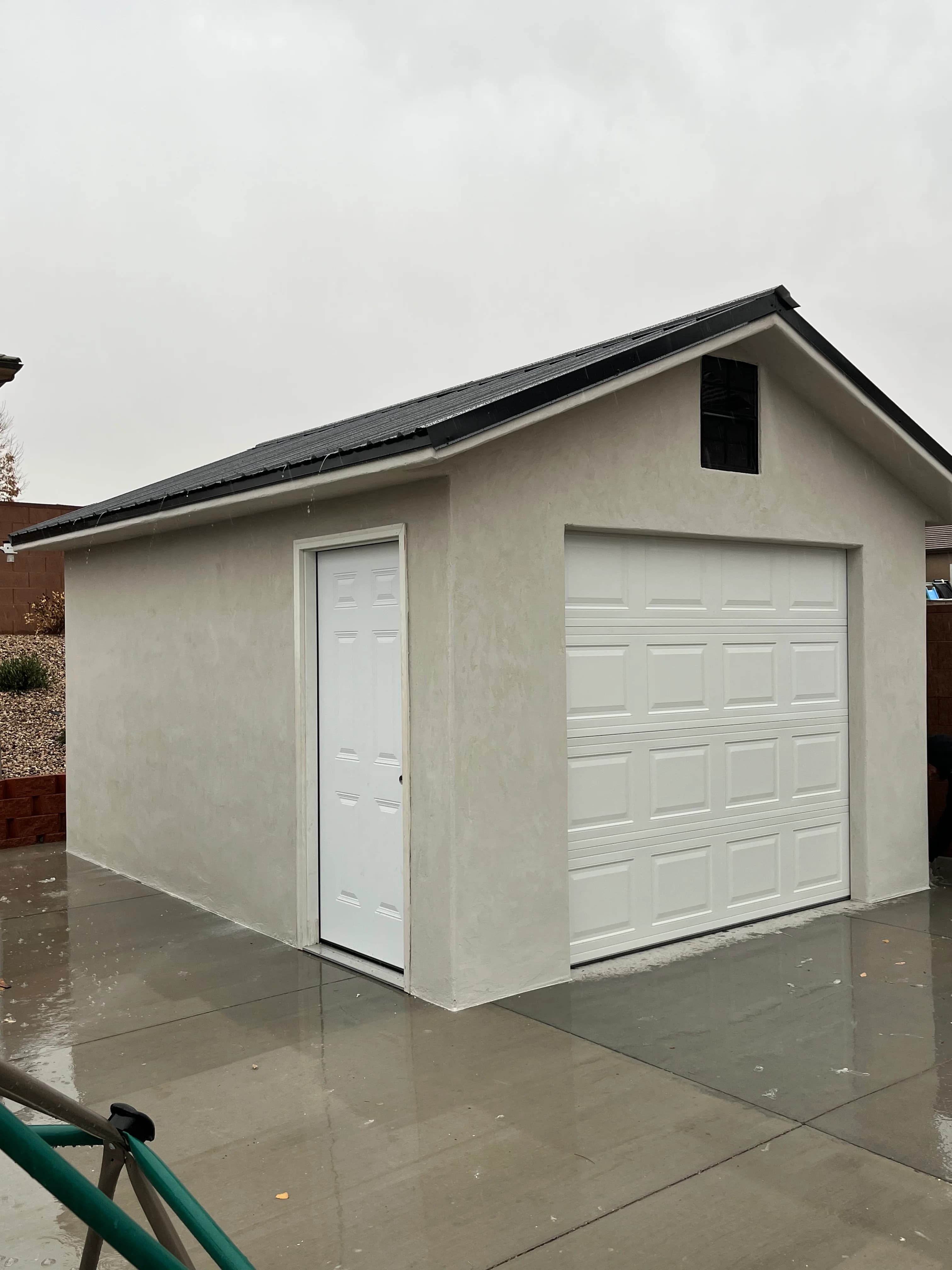 Stucco garage with white overhead door and entry door on concrete pad in a residential backyard