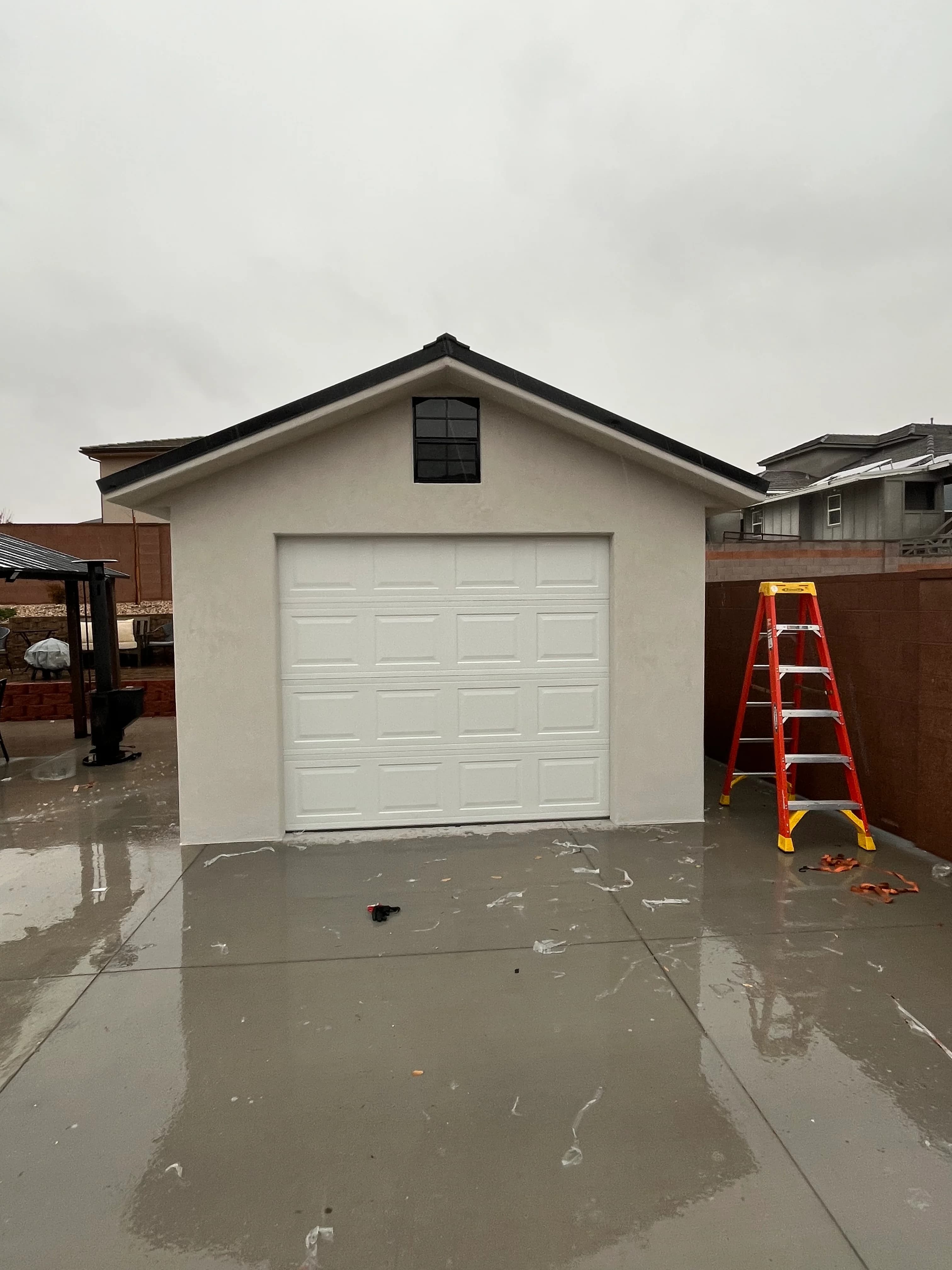 Finished detached garage with white stucco walls, sectional garage door, and dark metal roof by Quality Creations