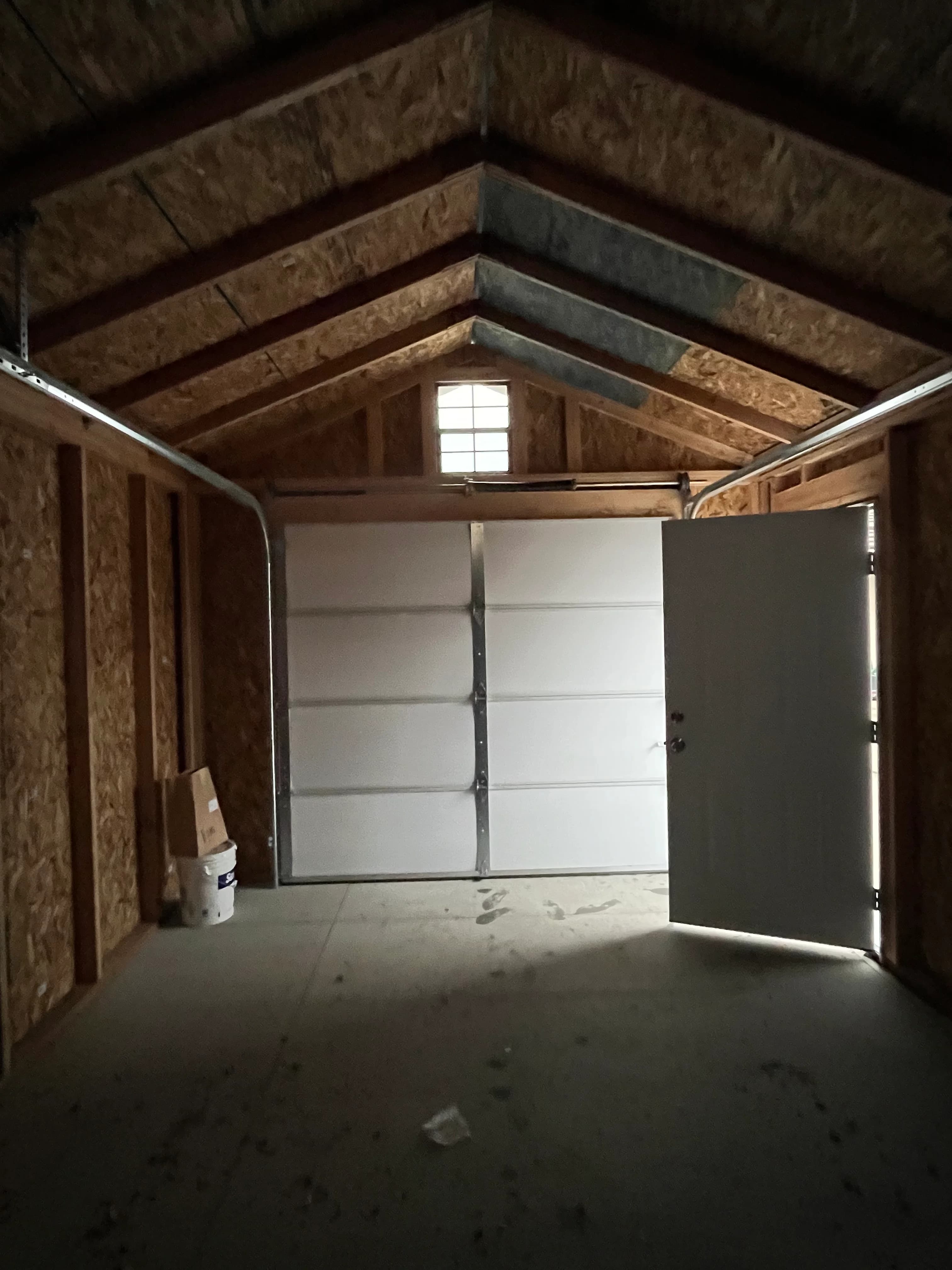 Interior of custom garage showing exposed wood framing, vaulted ceiling, overhead door, and entry door