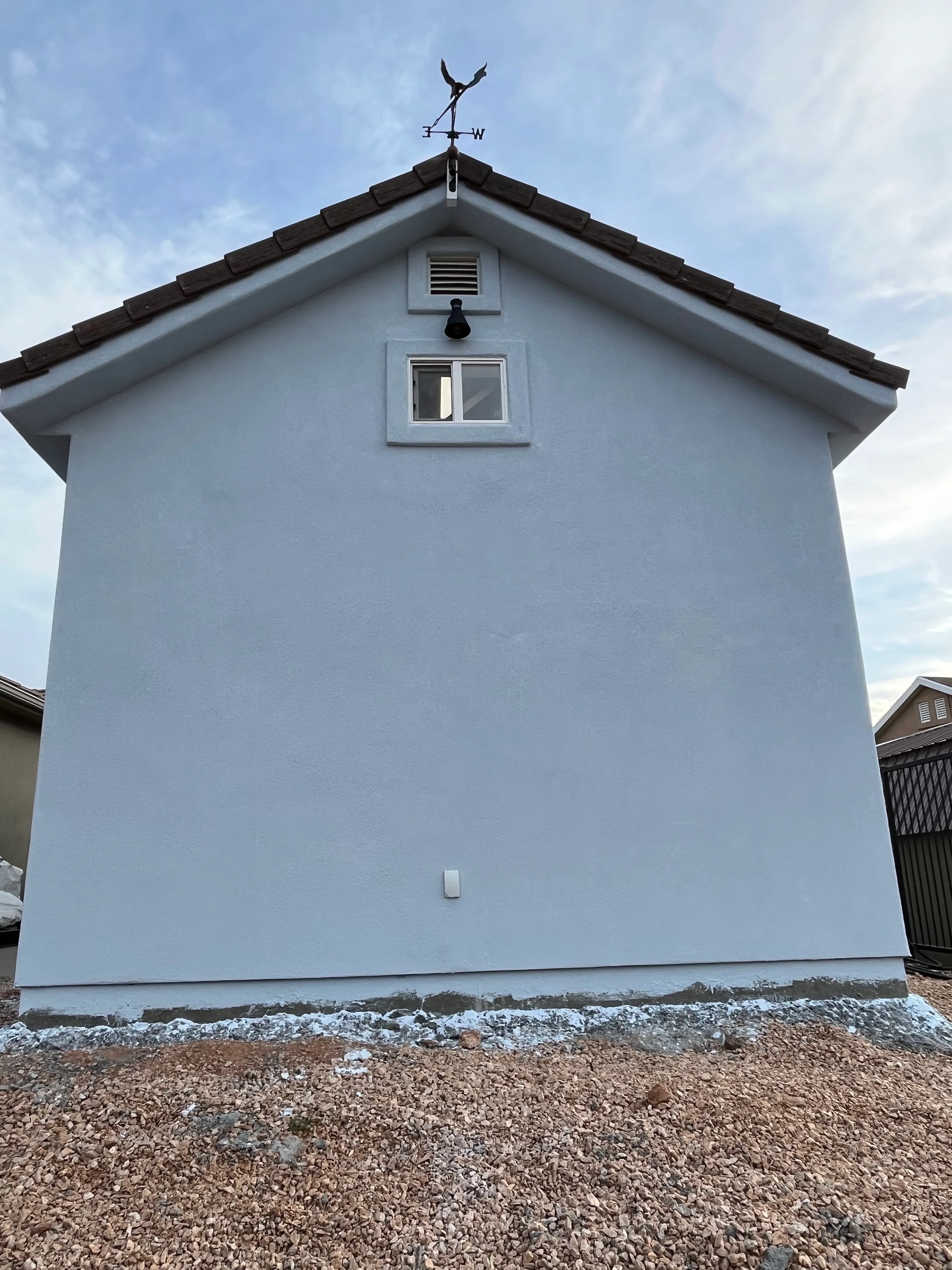 Rear view of two-story stucco garage with weather vane, gable vent, and upper window by Quality Creations