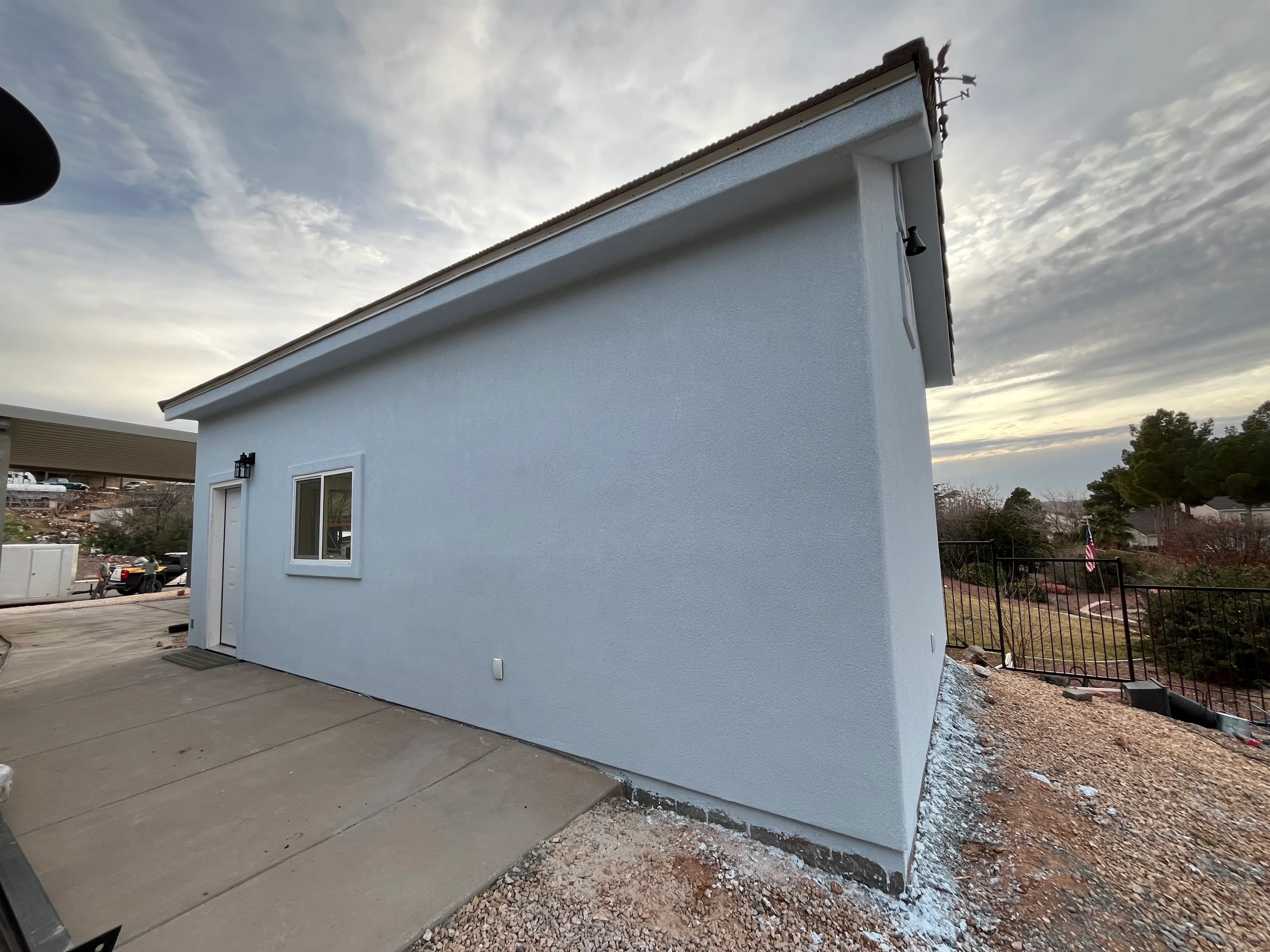Side view of white stucco detached garage with window and brown trim on a residential property