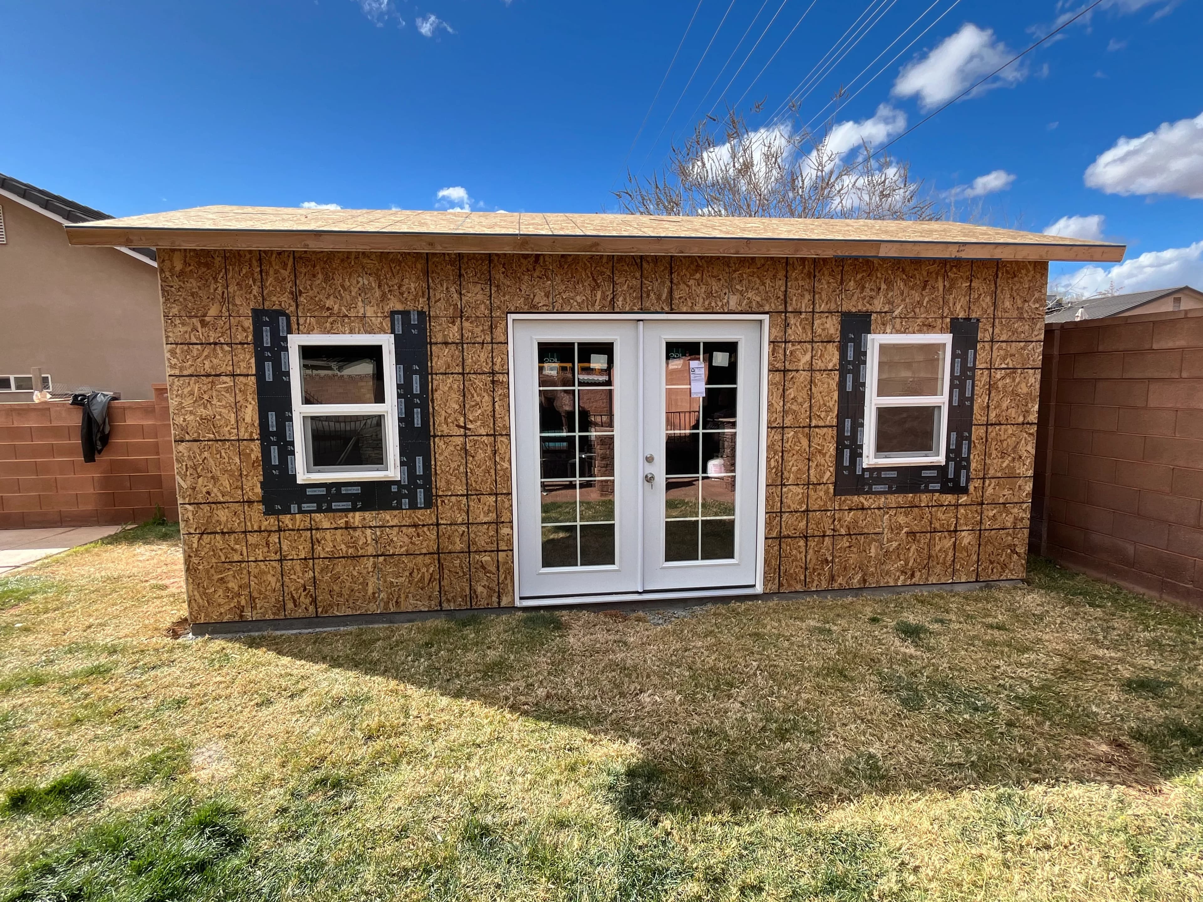 Custom backyard shed under construction with French doors, dual windows, and lean-to roof in Southern Utah