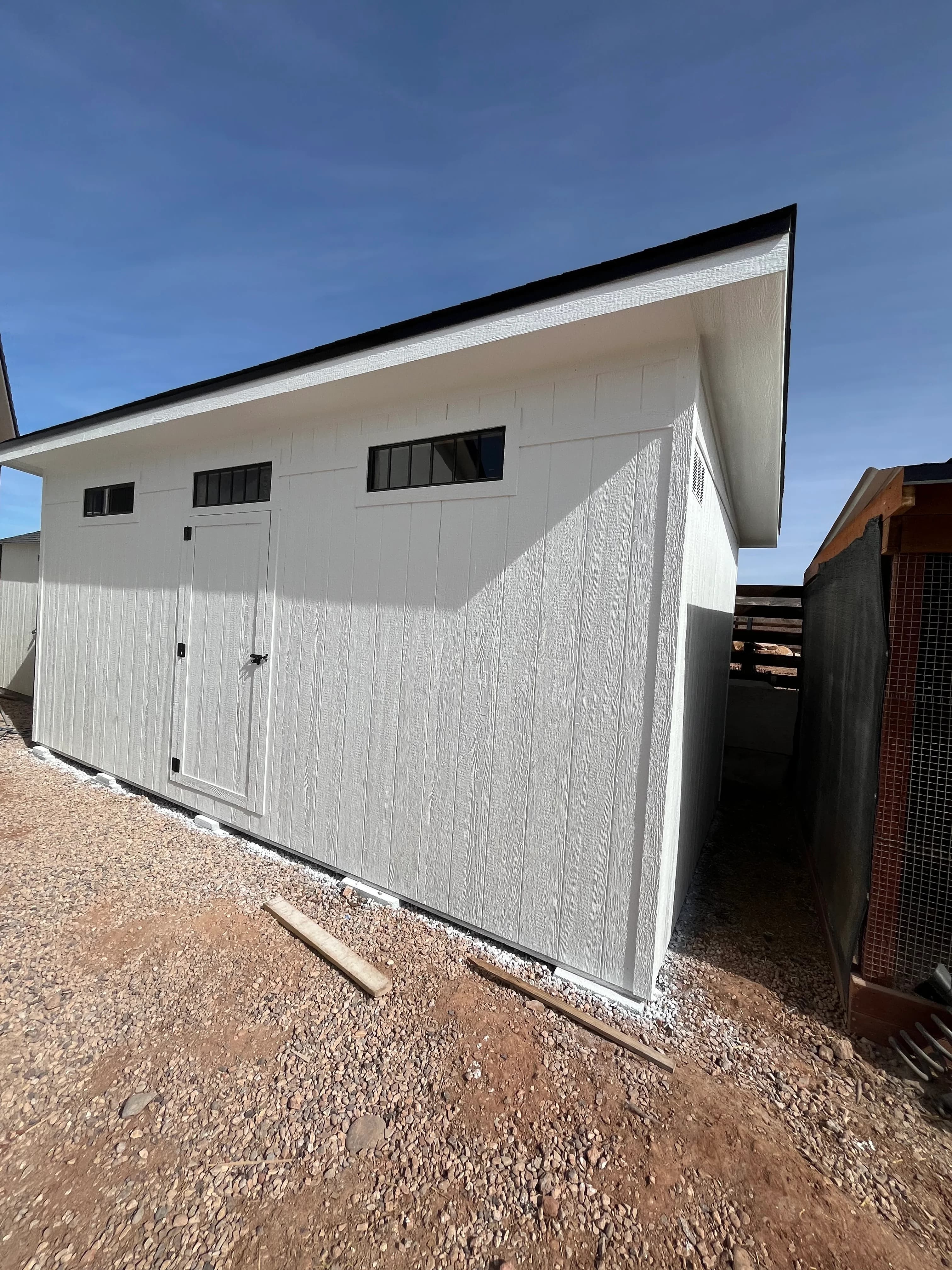 White contemporary storage shed with double doors, transom windows, and skillion roof in a Southern Utah backyard